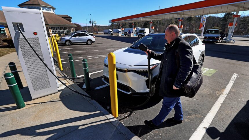 A middle-aged man prepares to plug his electric vehicle into a public charger at a filling station on the Massachusetts Turnpike.