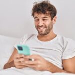 A happy guy sitting in bed reading on his phone.