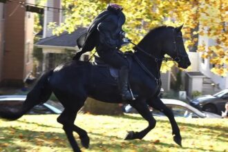 a rider in a headless horseman costume rides by yellow fall leaves