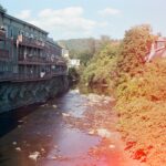 A film photo of a river near buildings with a sun spot on the right