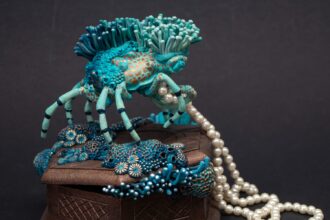 a sculpture made from a vintage box with a decorator crab on top, collecting a string of pearls and surrounded by blue coral