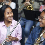 Confident Asian mixed race teenage girls playing brass instruments in classroom. Students are practicing music at high school. They are learning musical instruments.