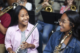 Confident Asian mixed race teenage girls playing brass instruments in classroom. Students are practicing music at high school. They are learning musical instruments.