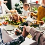 A family holding hands around a Thanksgiving dinner table.