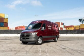 A maroon van sits in an empty lot in front of shipping containers