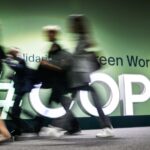 People walk past the logotype at the venue for the 2024 United Nations Climate Change Conference (COP29) in Baku on November 11, 2024.