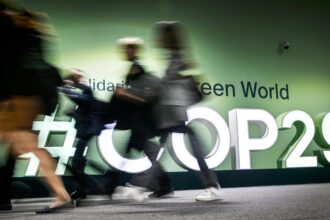 People walk past the logotype at the venue for the 2024 United Nations Climate Change Conference (COP29) in Baku on November 11, 2024.