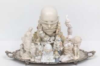 a sculpture made from found objects and figurines tied together with string atop a silver serving platter