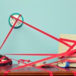 Image of a computer, phone and clock on a desk tied in red tape.