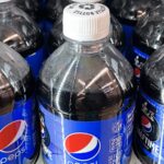 Three plastic bottles of Pepsi on a store shelf, side by side.