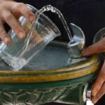 A close up on a drinking fountain, with a person filling a cup with water.