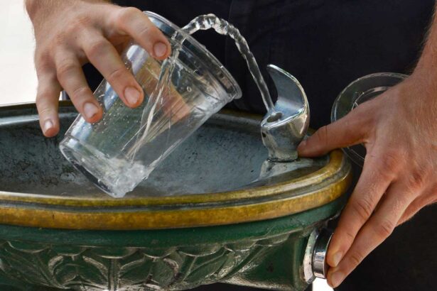 A close up on a drinking fountain, with a person filling a cup with water.