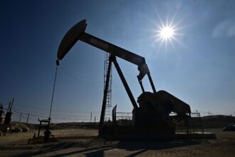 The sun burns brightly behind a dark pumpjack in an empty field