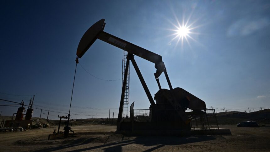 The sun burns brightly behind a dark pumpjack in an empty field