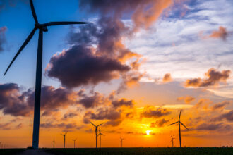 Wind turbines stand against a sunset near the Gulf of Mexico.