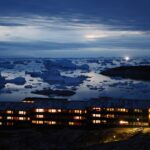 Icebergs float in Disko Bay, near a row of warmly illuminated houses, as moonlight shines through the clouds on September 03, 2021 in Ilulissat, Greenland.