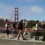 People walking on a san francisco sidewalk with the golden gate bridge in the background