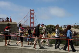 People walking on a san francisco sidewalk with the golden gate bridge in the background