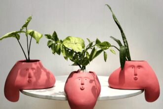 three pink blob-like vases that hang over the edge of a table. each holds leafy green plants and each has a face.