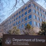 A large beige building with big dark grey windows looms over a department of energy sign