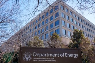 A large beige building with big dark grey windows looms over a department of energy sign