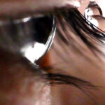 A closeup shows an eye framed by eyelashes, with four droplets of water pictured landing on an eyelash, sliding off, and falling.