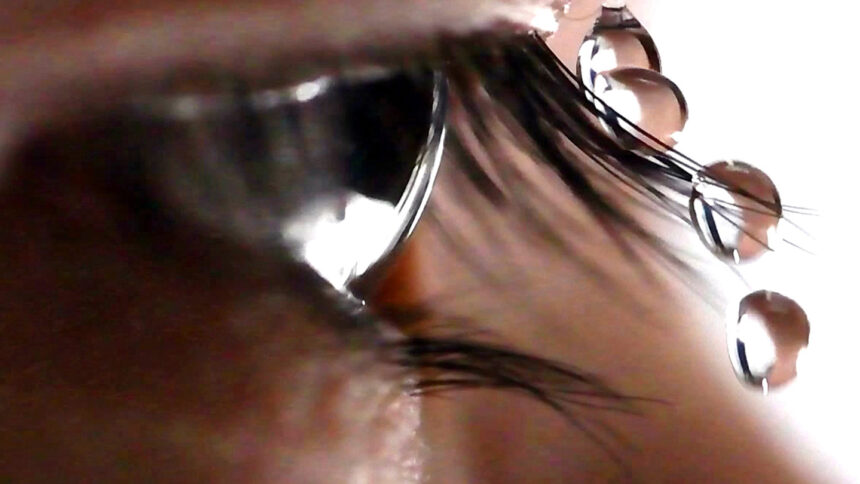 A closeup shows an eye framed by eyelashes, with four droplets of water pictured landing on an eyelash, sliding off, and falling.