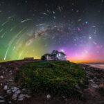 a glowing photograph of bright auroras, stars, and meteors over a mountain Croatian landscape with a house in the center