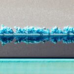 A horizontal line of bright blue crystals is reflected in liquid, underneath which is a teal line