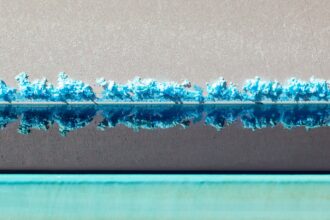 A horizontal line of bright blue crystals is reflected in liquid, underneath which is a teal line