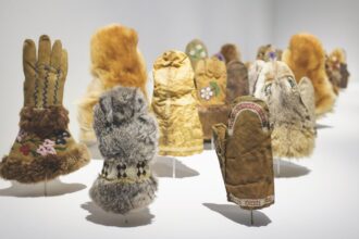 a detail of an installation of various handmade fur and seal skin mittens illuminated in a gallery