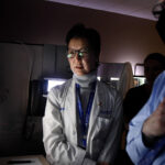 Shelley Hwang wears a lab coat. Her face is illuminated by light from a computer screen where she reviews results from breast cancer testing.