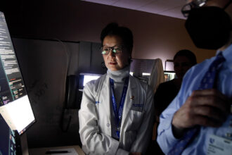 Shelley Hwang wears a lab coat. Her face is illuminated by light from a computer screen where she reviews results from breast cancer testing.