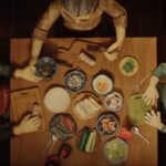 a screenshot from a stop-animated film short of an aerial view of a family around a table making spring rolls