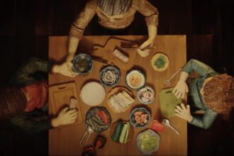 a screenshot from a stop-animated film short of an aerial view of a family around a table making spring rolls