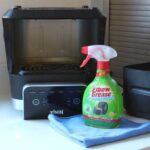 An air fryer turned upside down, with cleaning spray and a cloth in front of it