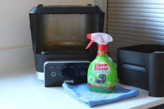 An air fryer turned upside down, with cleaning spray and a cloth in front of it