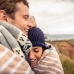 A couple hugging with blankets around them outside during fall.