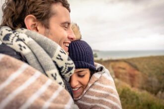 A couple hugging with blankets around them outside during fall.