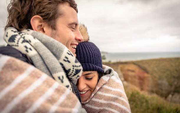 A couple hugging with blankets around them outside during fall.