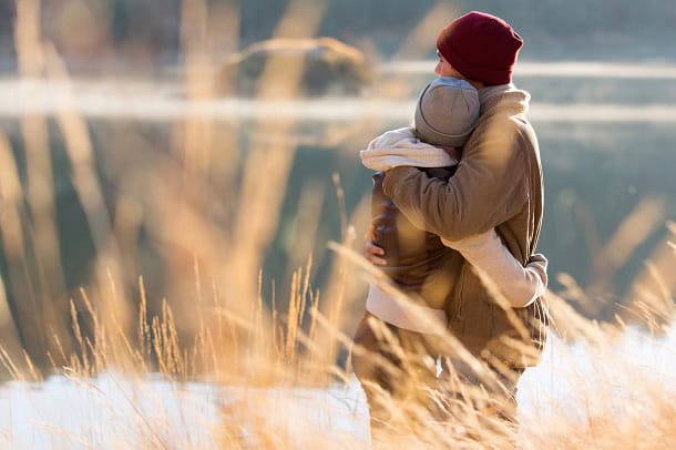 A couple embracing by a lake in the fall.