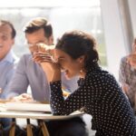 Coworkers laughing together while sitting around a table at work.