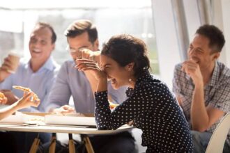 Coworkers laughing together while sitting around a table at work.