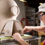 an artist works on a large almost figurative sculpture on a table