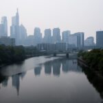 A gray skyline looms over a river in a sky filled with white smoke