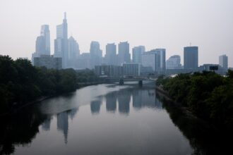 A gray skyline looms over a river in a sky filled with white smoke