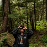 A man stands near old-growth trees as he looks for birds on his binoculars in the Tongass National Forest on Prince of Wales Island, Alaska.