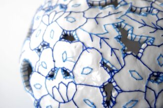 a detail of a white porcelain vessel embroidered with blue cotton thread