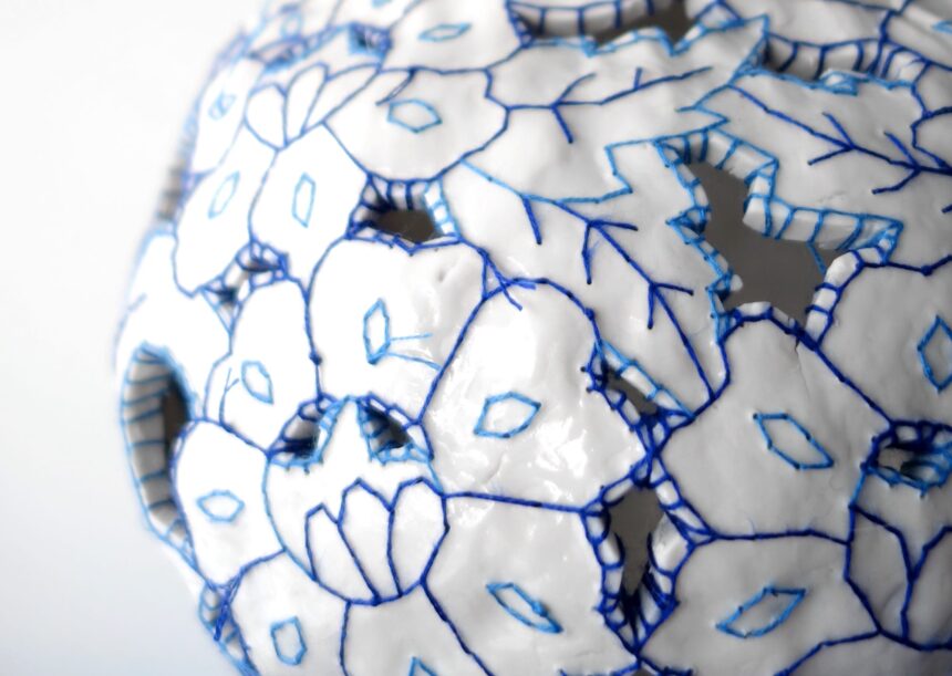 a detail of a white porcelain vessel embroidered with blue cotton thread