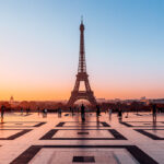 An orange sun reflects light on the smooth plaza in front of the Eiffel Tower in Paris.